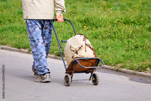 Man pushing a cart with a large beige bag on a city sidewalk