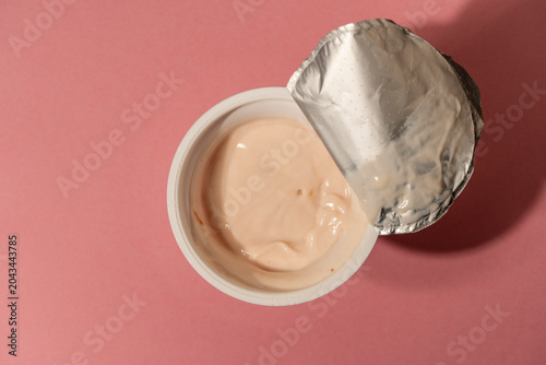 Fotografie Open plastic yogurt cup on pink background top view