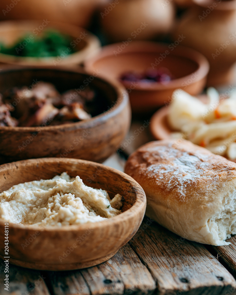 Fototapeta premium Cozy wooden bowls hold hummus, bread, and fresh herbs. Rustic table invites warm, comforting meals. Bread's soft crust promises tender taste. Gentle lighting highlights textures and warmth