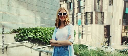 Fotografi Beautiful modern young woman looking at camera standing on city street in summer