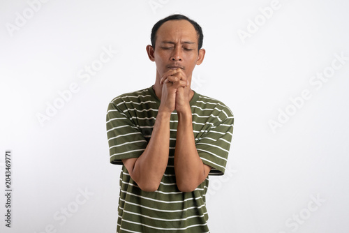 Asian man wearing green shirt with white stripes posing hoping and praying with his fists clenched in front of his face.