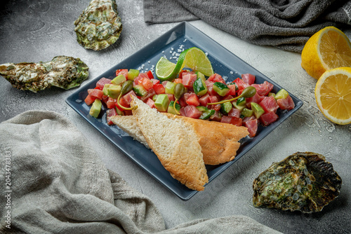 Fresh tuna tartare with avocado, cucumber, tomato, lime, capers and toasted bread served on a gray restaurant plate