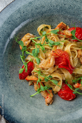 Top view of seafood tagliatelle with shrimp, cherry tomatoes and pea shoots served in a textured ceramic bowl for restaurant menu