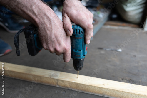 Bild auf Leinwand A close-up of a man's hands using a cordless drill to screw into a wooden plank