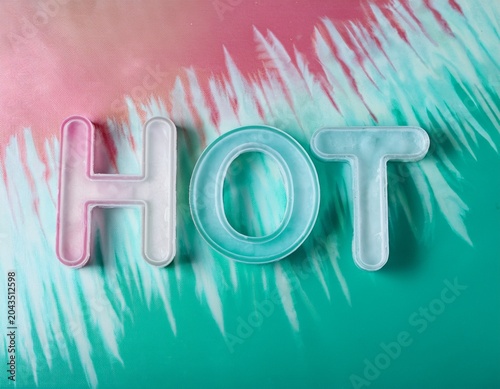 Top view of HOT 3D letters made with ice on pale green mint and pink tie and dye background with pink popsicles and copy space