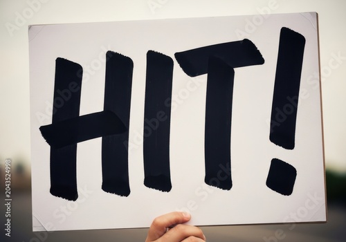 Hand holding a sign with the word hit written in bold black letters