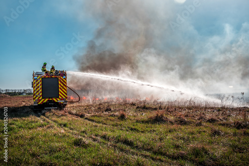 Foto Fire truck spraying water to extinguish a wild grass fire in a dry rural field