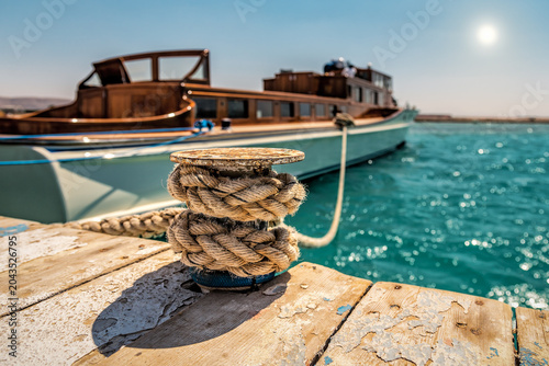 Close-up of a wooden pier with a bollard and ropes against the background of a luxury yacht. Travel and vacation theme