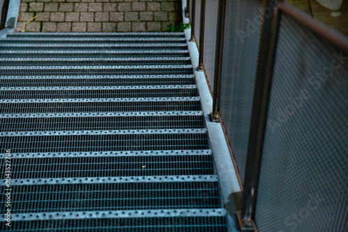 a professional high angle photograph of industrial metal stairs with railings leading down to cobblestone pavement