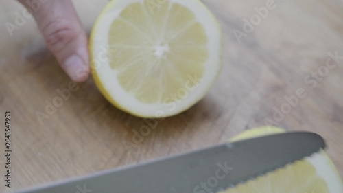 Hand slicing fresh ripe lemon with sharp knife on wooden cutting board. Juicy citrus rounds reveal pulp detail in natural light. Cooking and healthy food preparation concept.
