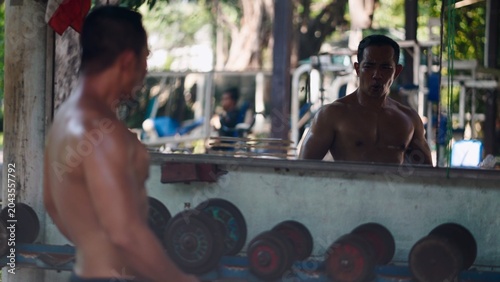 Bild auf Leinwand Asian man concentrating on strength training, seeing reflection at outdoor gym