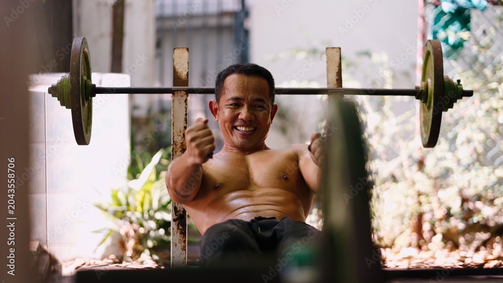 Fototapeta premium Smiling asian man successfully completing a strength workout with weights outdoors