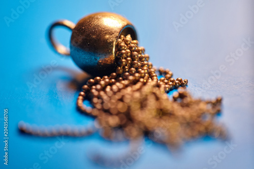 Conceptual macro shot of a golden ball chain spilling out of a metallic sphere. Golden bead chain flowing on a bright blue background.