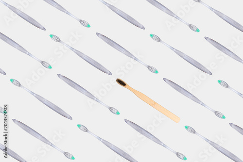 Bamboo toothbrush standing out from transparent plastic toothbrush pattern on gray background