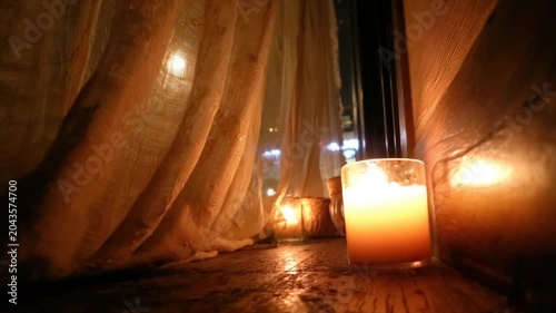 Warm candlelight illuminates a wooden surface, with a window and sheer curtains in the background