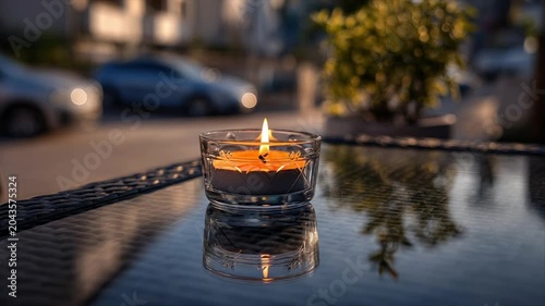 A lit candle in a glass votive sits on a glossy table, reflecting the flame