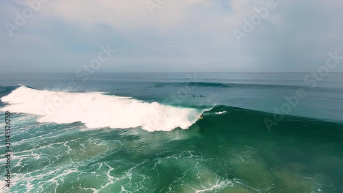 Aerial drone view of surfers, surfing paddling, duck diving, with beautiful blue collars and glass sea