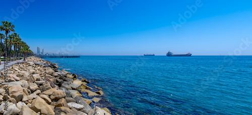 View along the coastal promenade from Limasol to the horizon with cargo ships under a blue sky and with blue sea, Cyprus