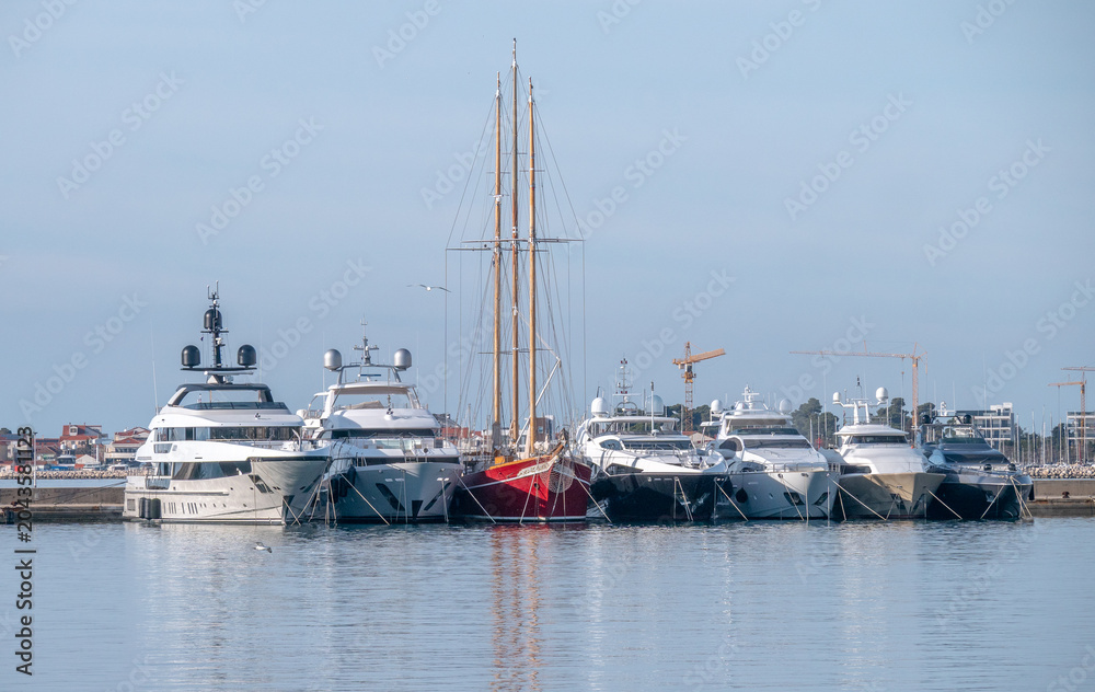 Fototapeta premium Classic Three Masted Sailing Yacht Moored Between Modern Motor Yachts in Harbor