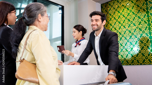Canvastavla Smiling male receptionist in elegant suit welcoming an elderly Asian female gue