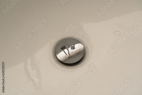 Round chrome click-clack drain stopper inside a beige ceramic sink or bathtub