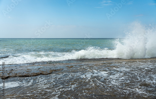 Powerful ocean wave crashing against a flat rocky shore