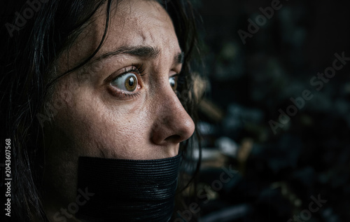 Terrified woman gagged with black tape in a dark close-up profile