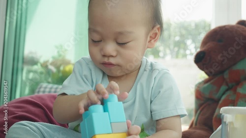 A young child is focused on stacking vibrant building blocks, showcasing creativity and early learning. The environment is cozy, filled with soft toys, encouraging exploration and imaginative play.