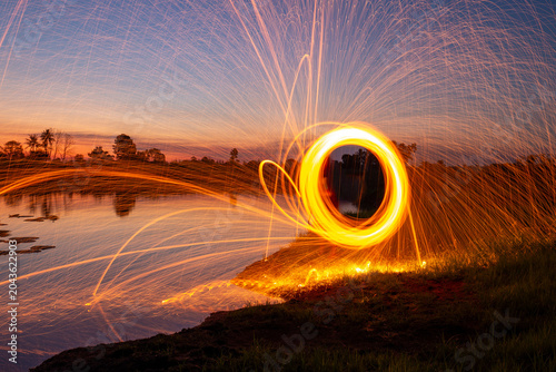 Tableau sur toile Spectacular steel wool spinning creating bright flying sparks over a calm lake during a golden sunset