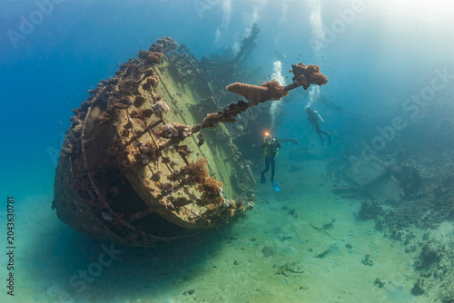Fotografie Cinematic underwater view of deep sea scuba diving excursion around an old coral overgrown ship wreck in clear blue ocean water