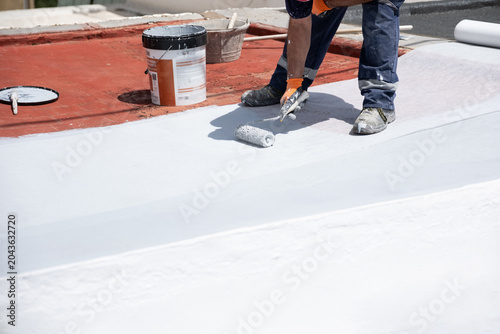 Fotografie Worker applying white liquid membrane coating a roof surface for waterproofing