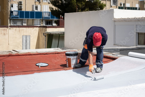 Canvas Print Worker applying white liquid membrane to a red roof surface using a roller