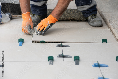 Tiler hands installing ceramic floor tiles using wedges and clips for even surface