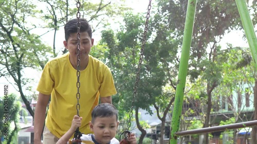 Happy Asian father gently pushing his little son on a playground swing at the park