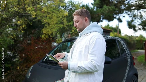 Portrait of a smiling young caucasian man holding a paper guide map and a coffee cup while standing next to his car during an autumn road trip journey