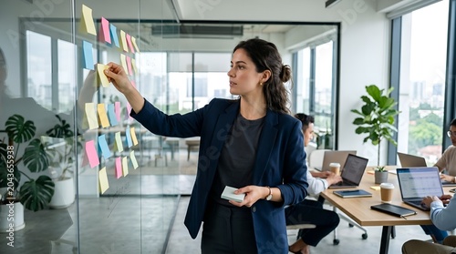 Businesswoman organizing colorful sticky notes on office glass wall