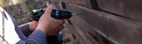 Billede på lærred Man using cordless drill to screw wooden fence board
