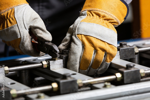 Bild auf Leinwand Close-up of hands wearing work gloves tightening a bolt with pliers on machinery