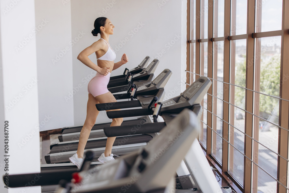 Fototapeta premium Young woman running on treadmill in a modern fitness gym, engaging in cardio workout for health and wellness