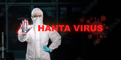 Fotografía Healthcare professional in white PPE coverall and blue gloves raises a stop hand gesture warning against hantavirus exposure inside a dimly lit rural health clinic