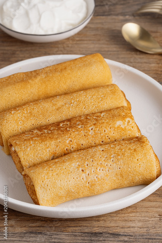 Delicious rolled pancakes served with cream on a wooden table