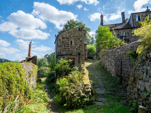 Beautiful old stone houses in Hollins a hamlet on the outskirts of Hebden Bridge on a cobbled land surrounded by summer trees and flowers