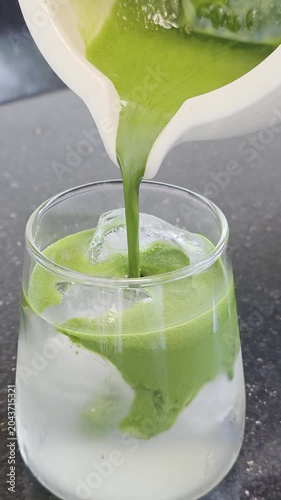 Pouring green matcha latte into a glass with ice cubes