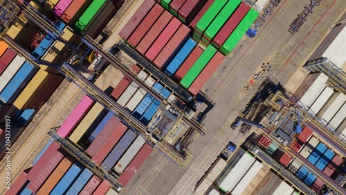 Impressive top-down aerial perspective showing gantry cranes moving and stacking colorful shipping containers in a busy industrial port terminal, showcasing the global logistics and trade industry