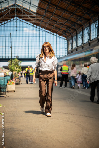 Картината върху платно Elegant mid-adult woman walking on a train station platform, business travel con