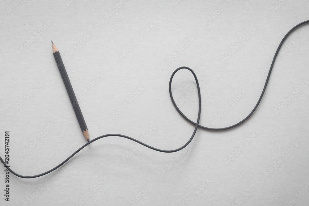 Obraz premium A pencil lies next to a long, curved black cord on a plain surface.