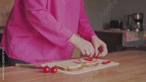 A woman stuffs a sandwich with sausage and tomatoes. Cooking at home.