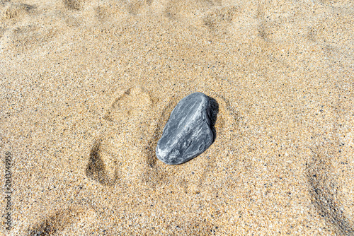A single textured grey stone isolated on beach sand. A symbol of strength, individuality, and persistence. Minimalist natural background with authentic sunlight and soft shadows