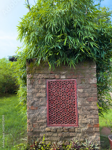 Traditional rustic clay brick village hut. Ornate red window. Bamboo foliage vegetation, rural Indian architecture heritage, countryside tranquility, earthen construction and natural home garden lands