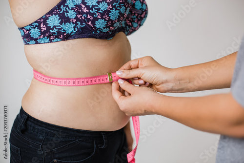 Fotografía Close up of female hands measuring overweight woman waist size with pink soft tape measure